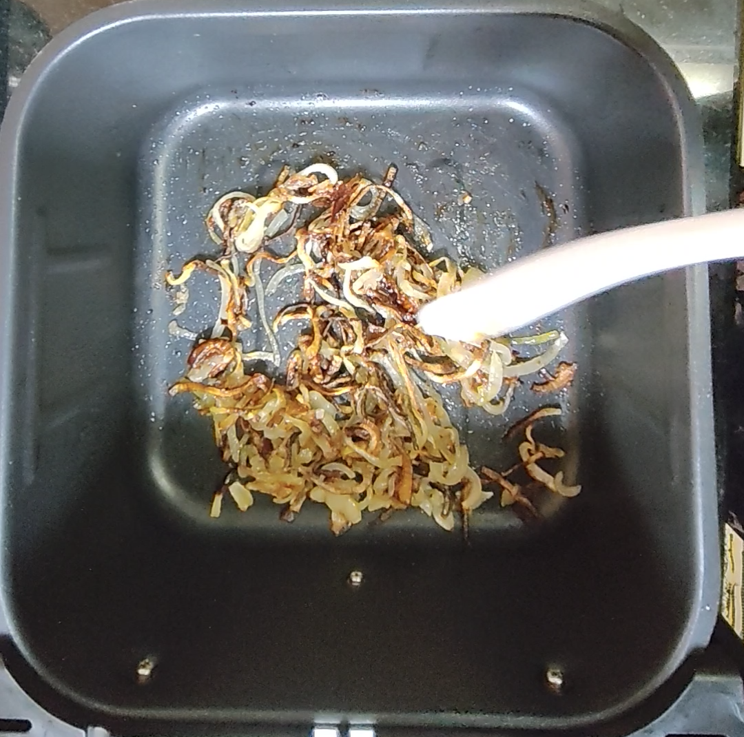 Browned sliced onions with darker crisp edges in an air fryer basket after cooking