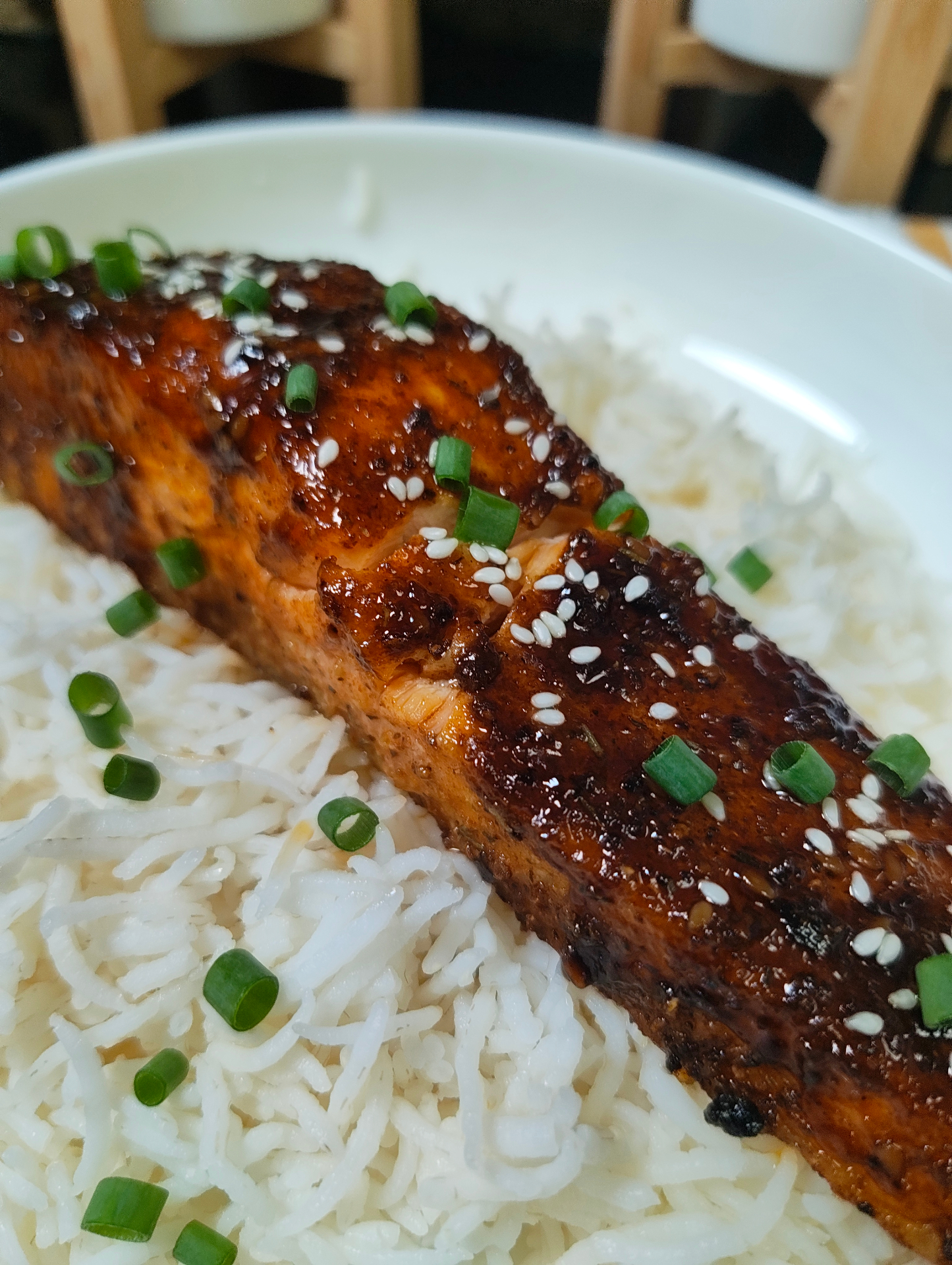 Close view of a glazed salmon fillet over white rice, topped with sesame seeds and chopped green onions