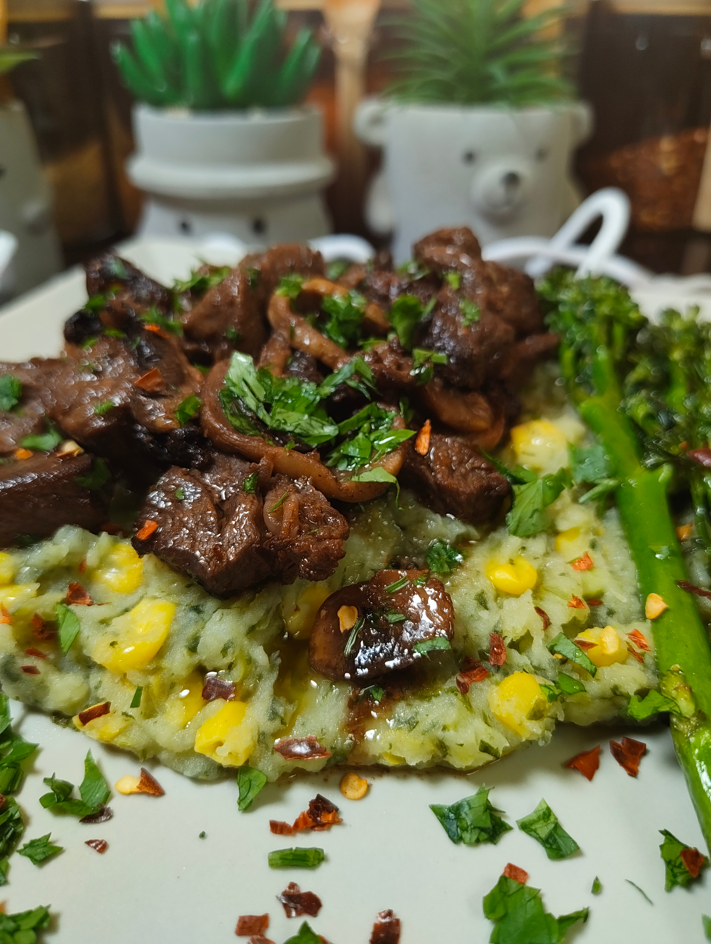Mukimo on a plate topped with air fryer beef and mushrooms and chopped parsley, with tenderstem broccoli alongside