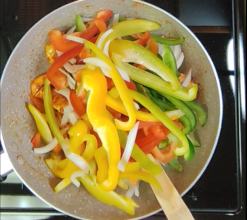 Red, yellow and green bell pepper strips cooking in a pan