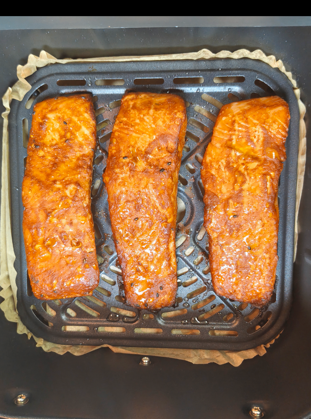 Three cooked salmon fillets in an air fryer basket