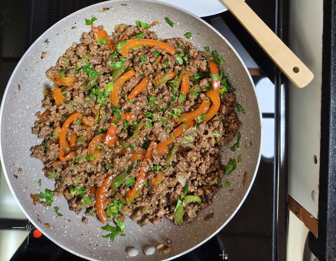 Cooked minced beef with sliced red and green bell peppers and fresh coriander in a light-coloured pan