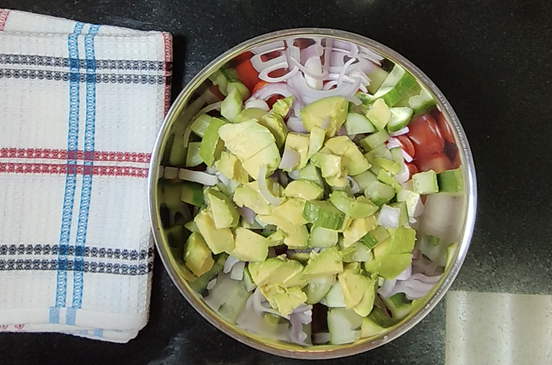 Chopped avocado, cucumber, sliced onion and halved cherry tomatoes combined in a metal bowl