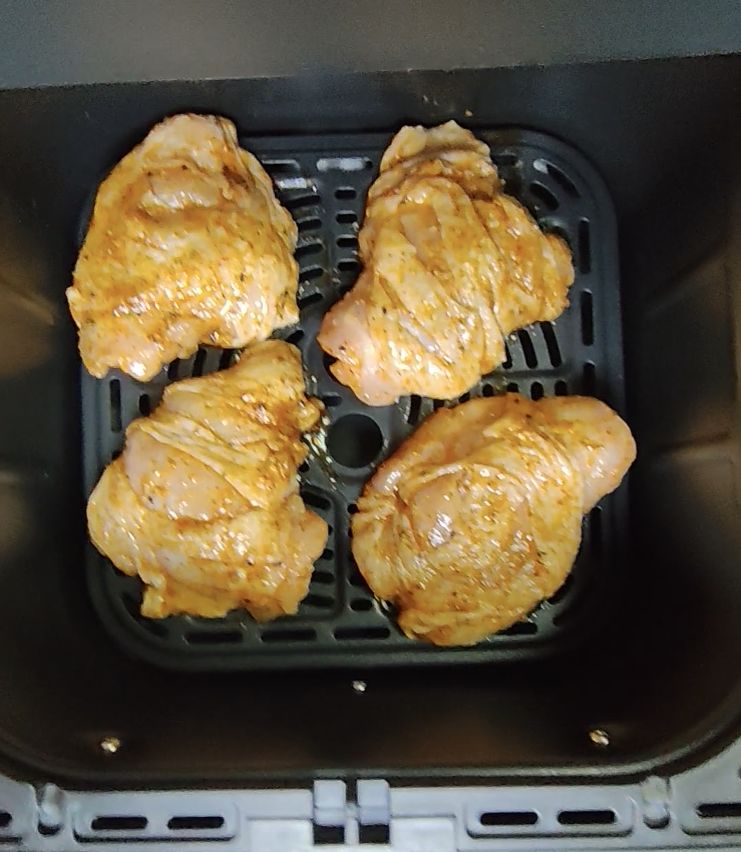 Four uncooked seasoned chicken thighs in an air fryer basket