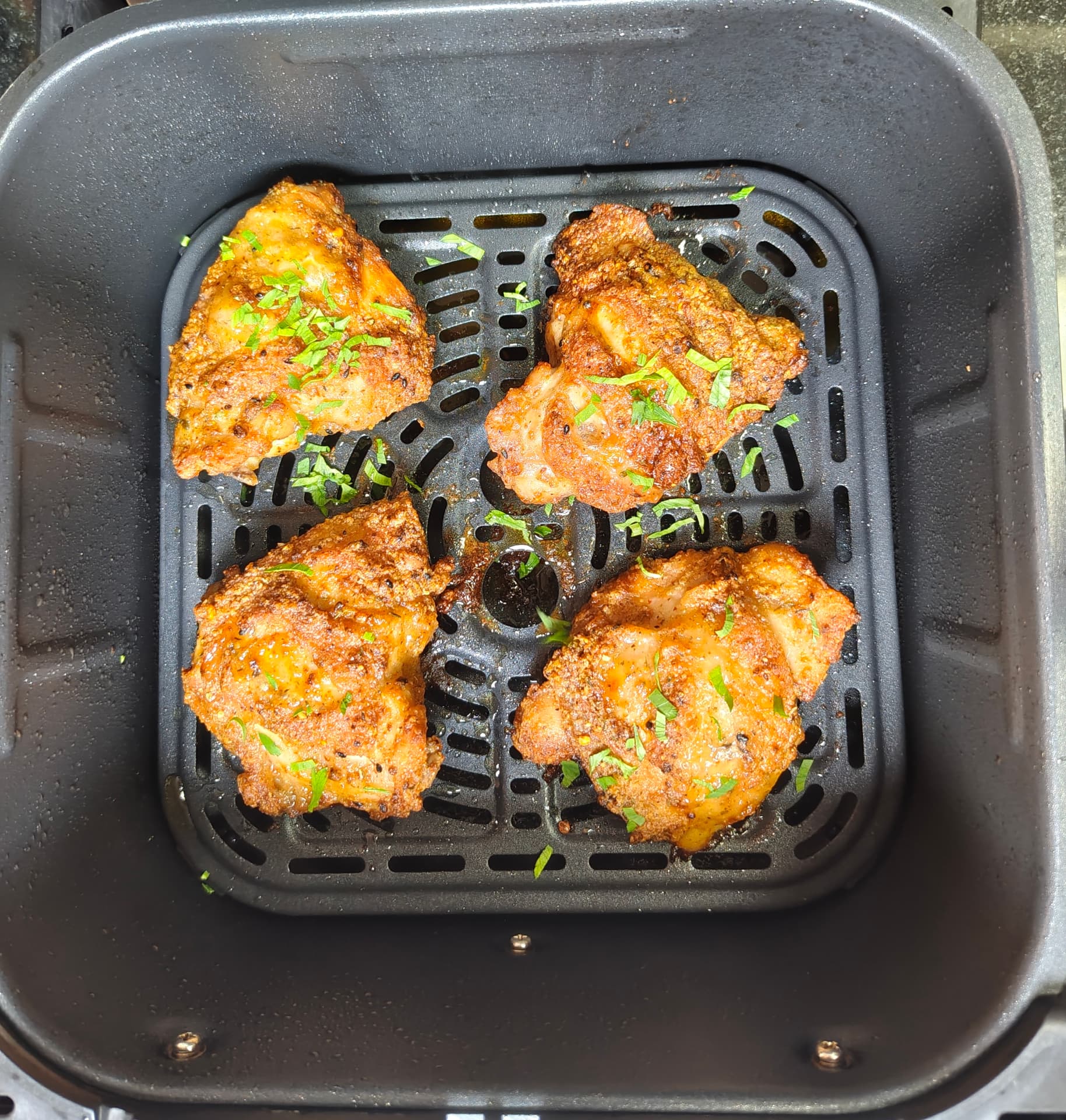 Four golden crispy chicken thighs in a single layer in an air fryer basket
