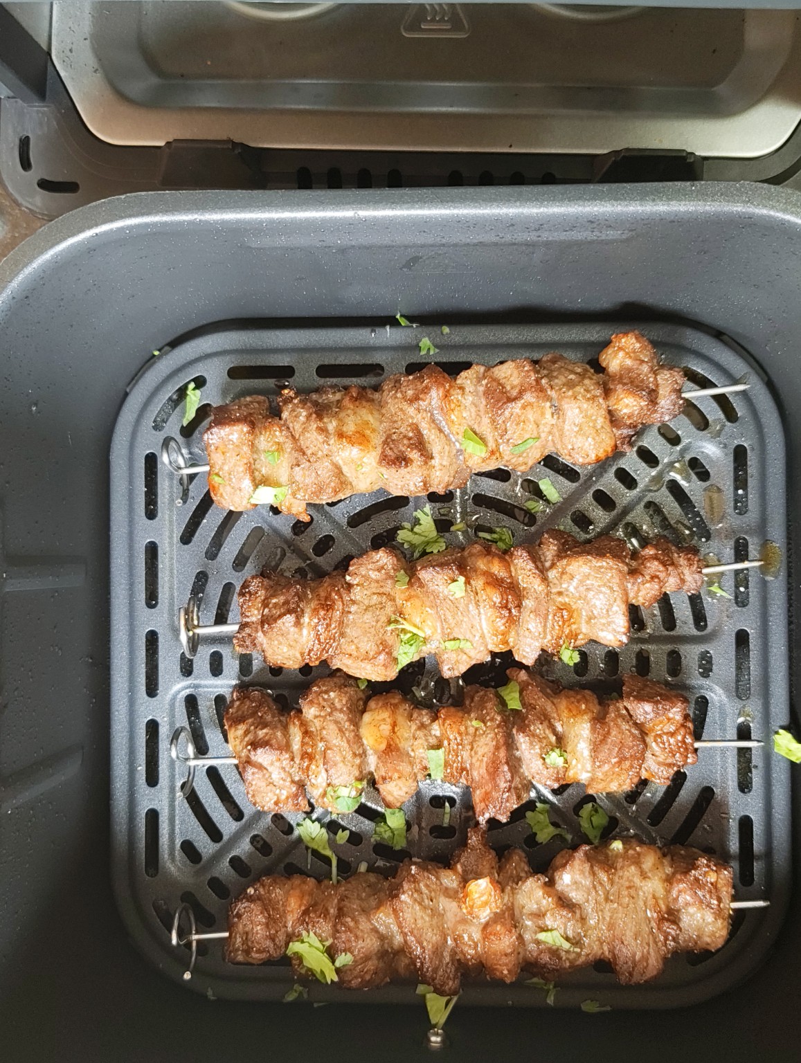 Four cooked beef skewers in an air fryer basket