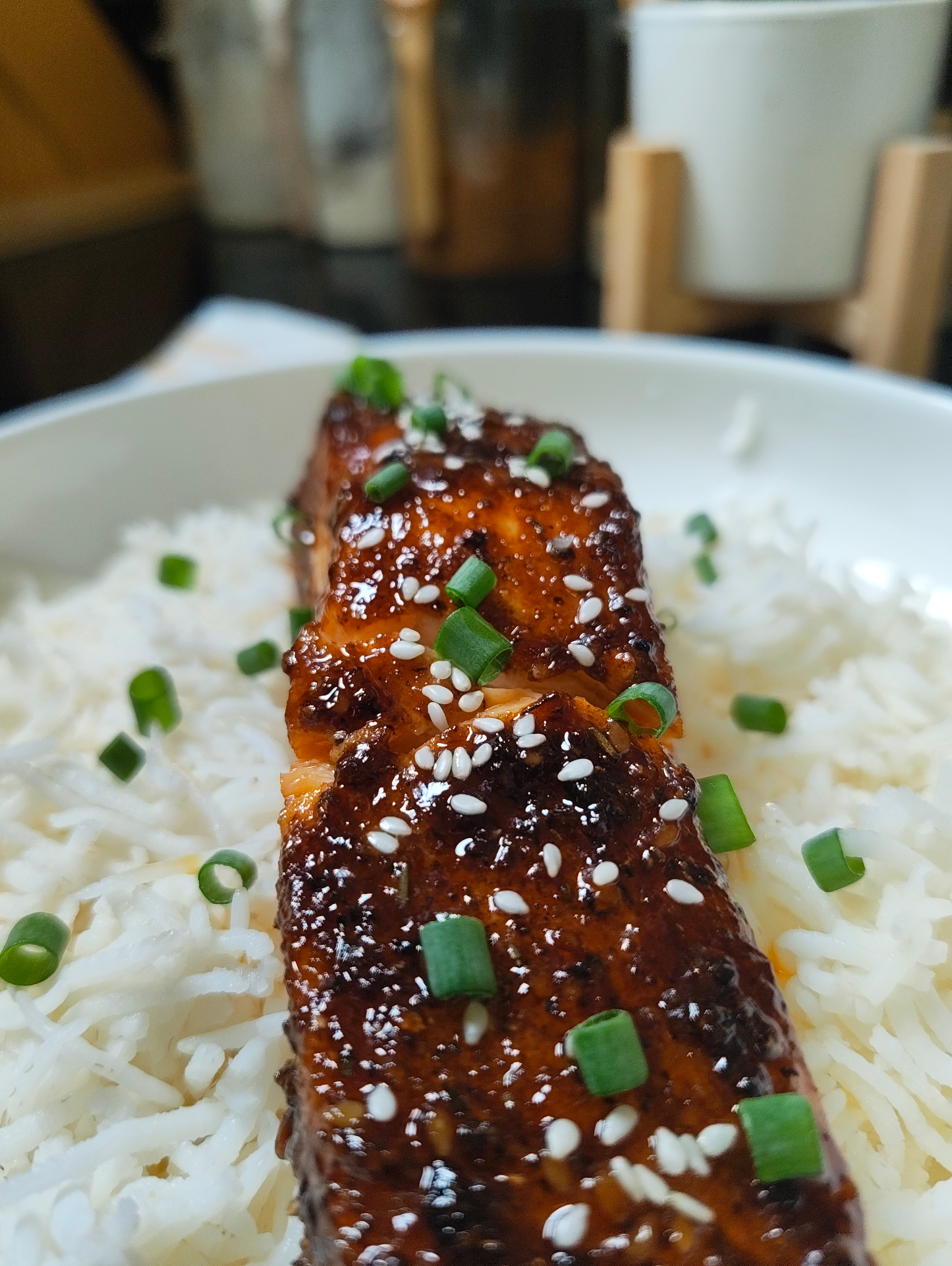 Angled close-up of a glazed salmon fillet on white rice with sesame seeds and green onions