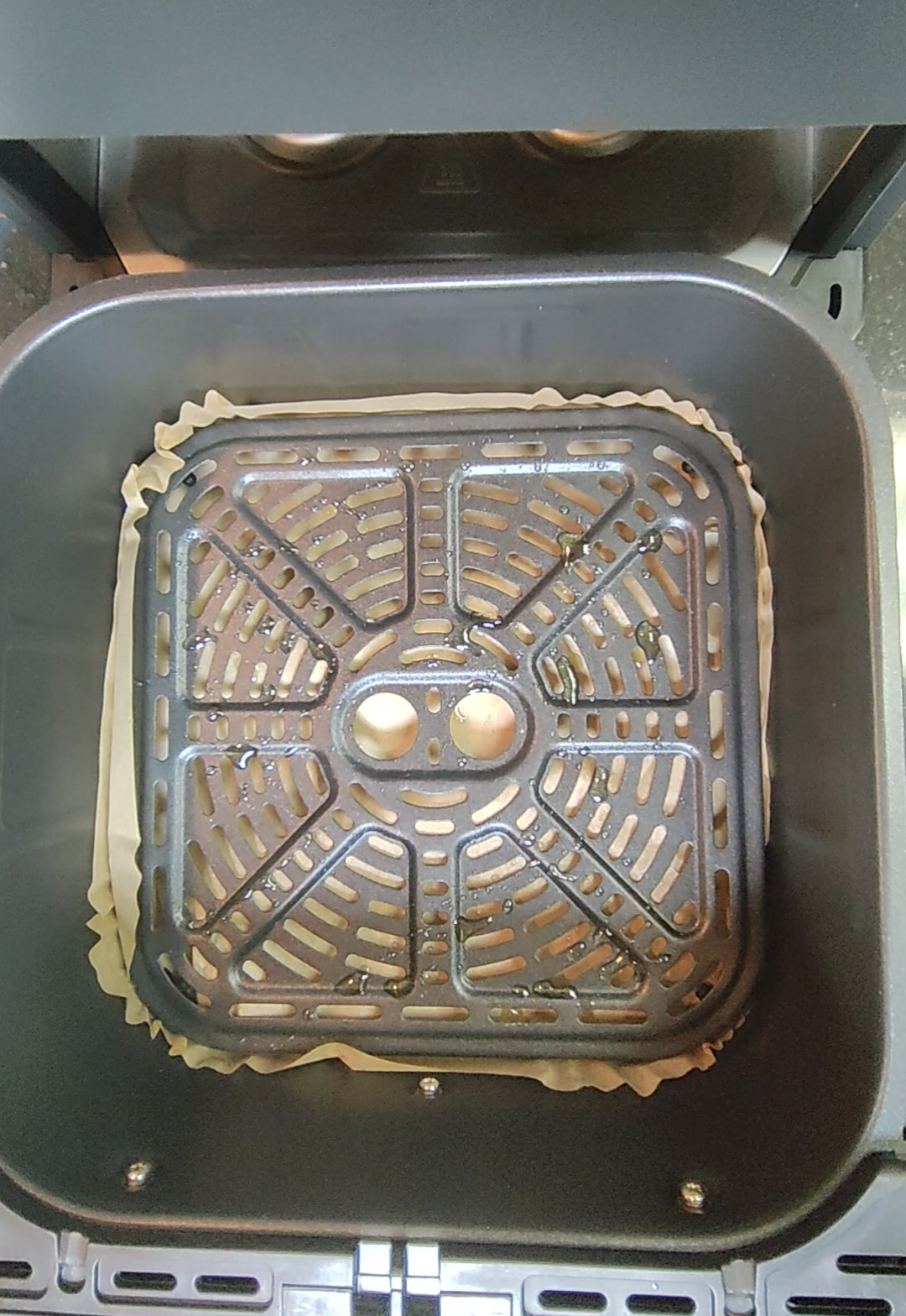 Air fryer basket with crisper plate and parchment liner after cooking