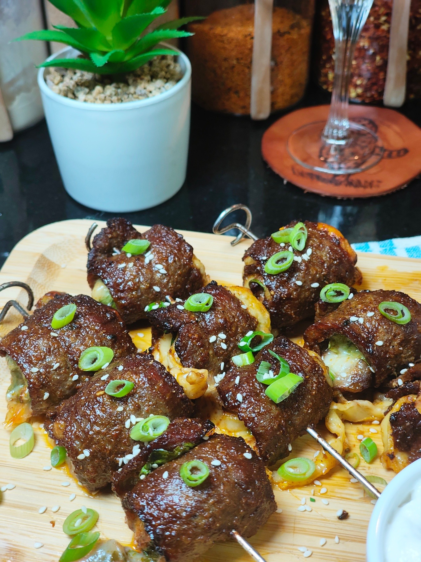 Close-up of browned spinach and mozzarella stuffed beef skewers with melted cheese, sesame seeds and spring onions on a wooden board