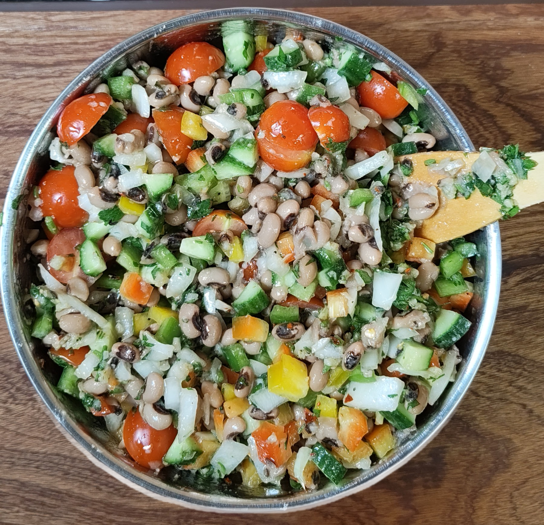 Finished black eyed peas salad with cucumber, cherry tomatoes, colourful bell peppers, white onion and parsley dressing in a metal bowl