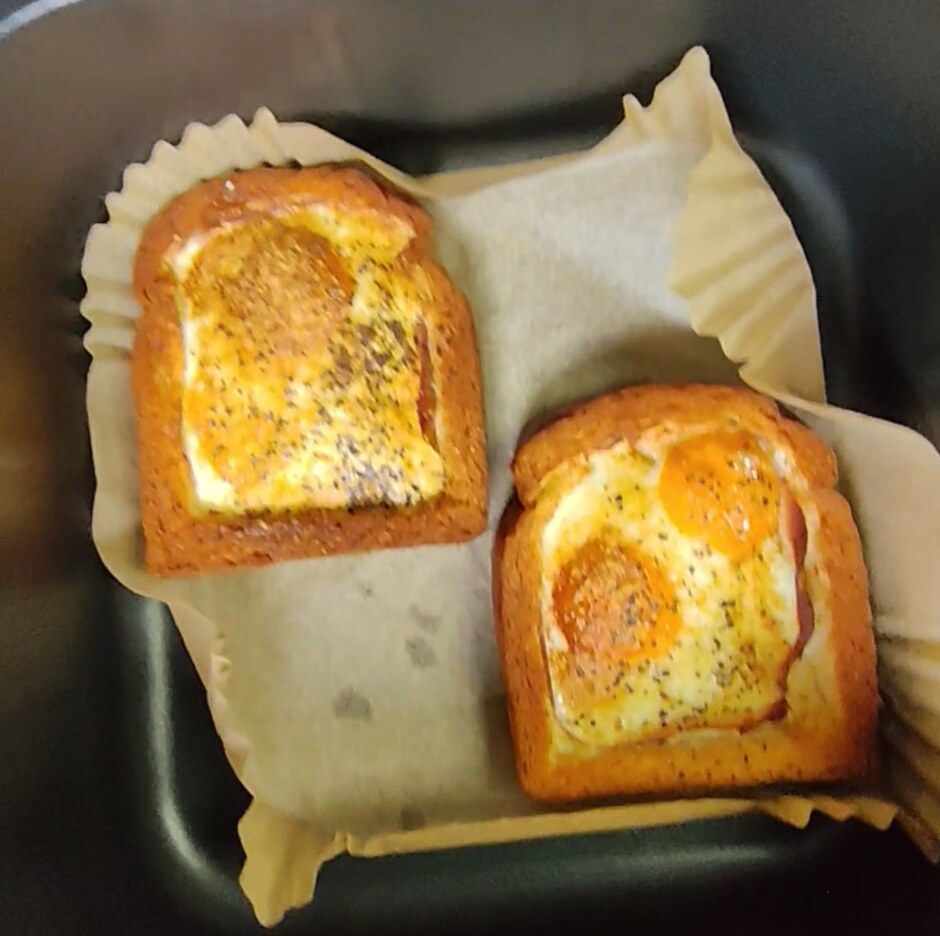 Two golden eggs in a hole with set eggs and black pepper in an air fryer basket on a liner
