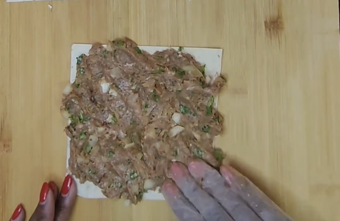 Beef mixture being spread over a square of tortilla