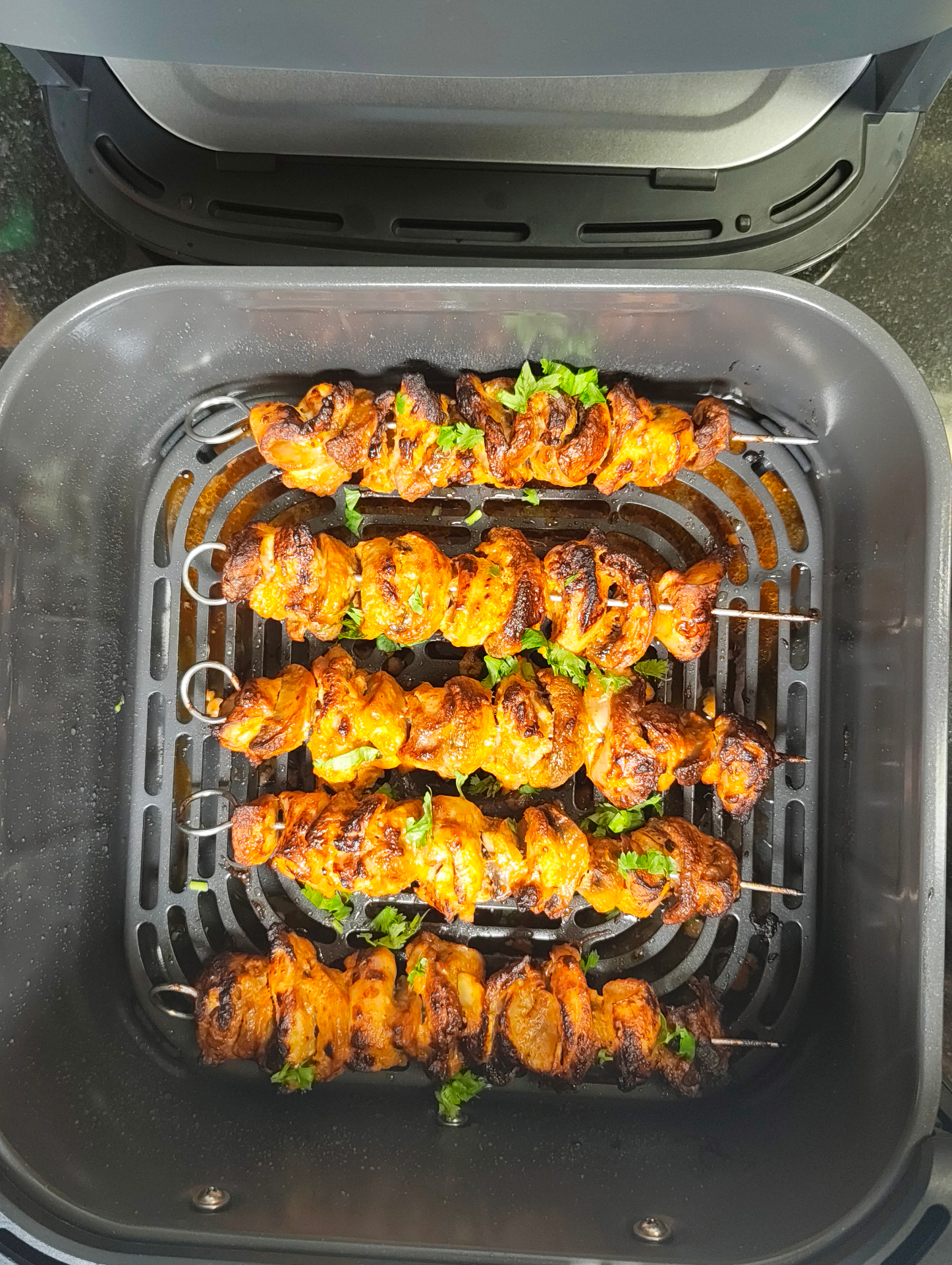 Browned meat skewers sprinkled with fresh herbs cooking in an air fryer basket