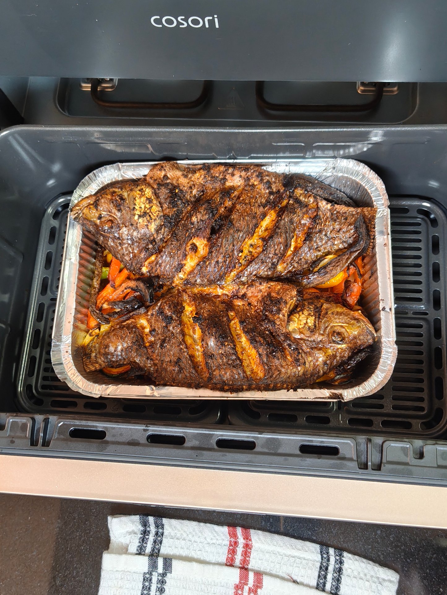 Two whole tilapia cooked in an air fryer, browned and scored, in a foil tray in the basket