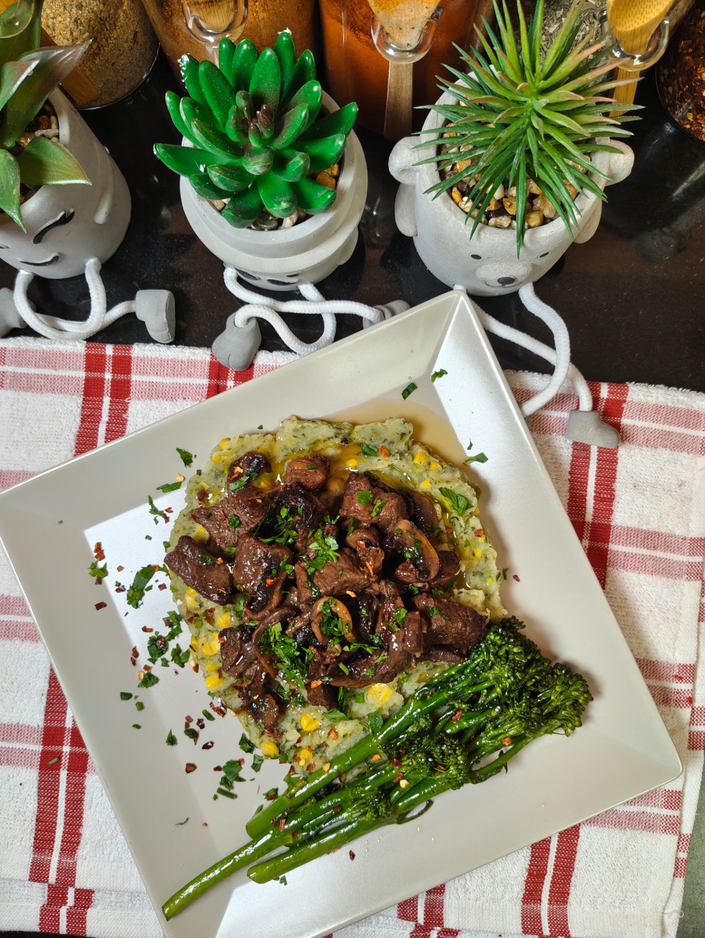 Air fryer beef cubes and mushrooms topped with chopped parsley over mokimo on a white square plate, with tenderstem broccoli on the side