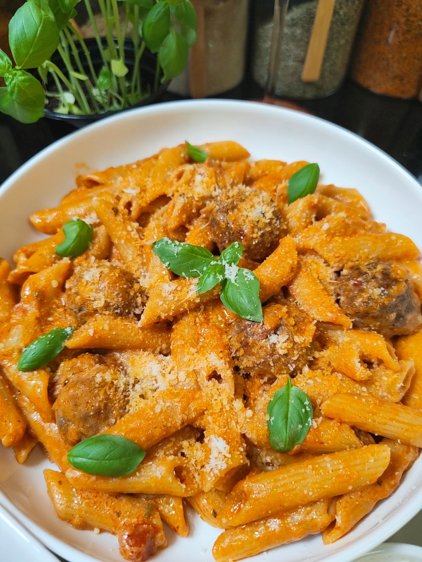 Close view of penne and meatballs finished with Parmesan and fresh basil
