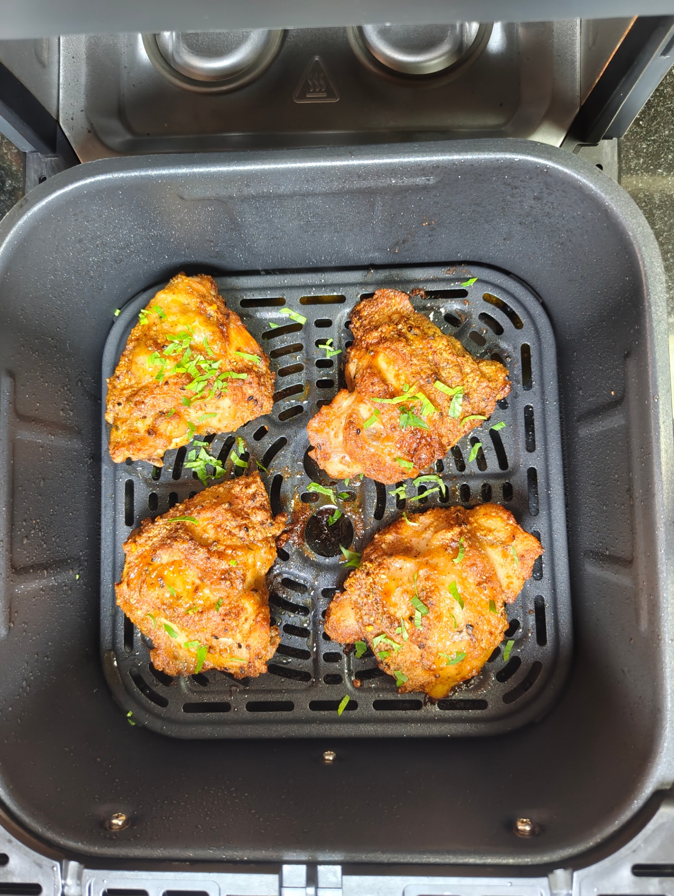 Golden crispy chicken thighs in an air fryer basket, sprinkled with chopped herbs