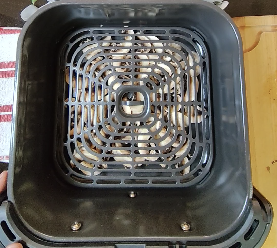 Sliced white mushrooms visible beneath the crisper plate inside an air fryer basket