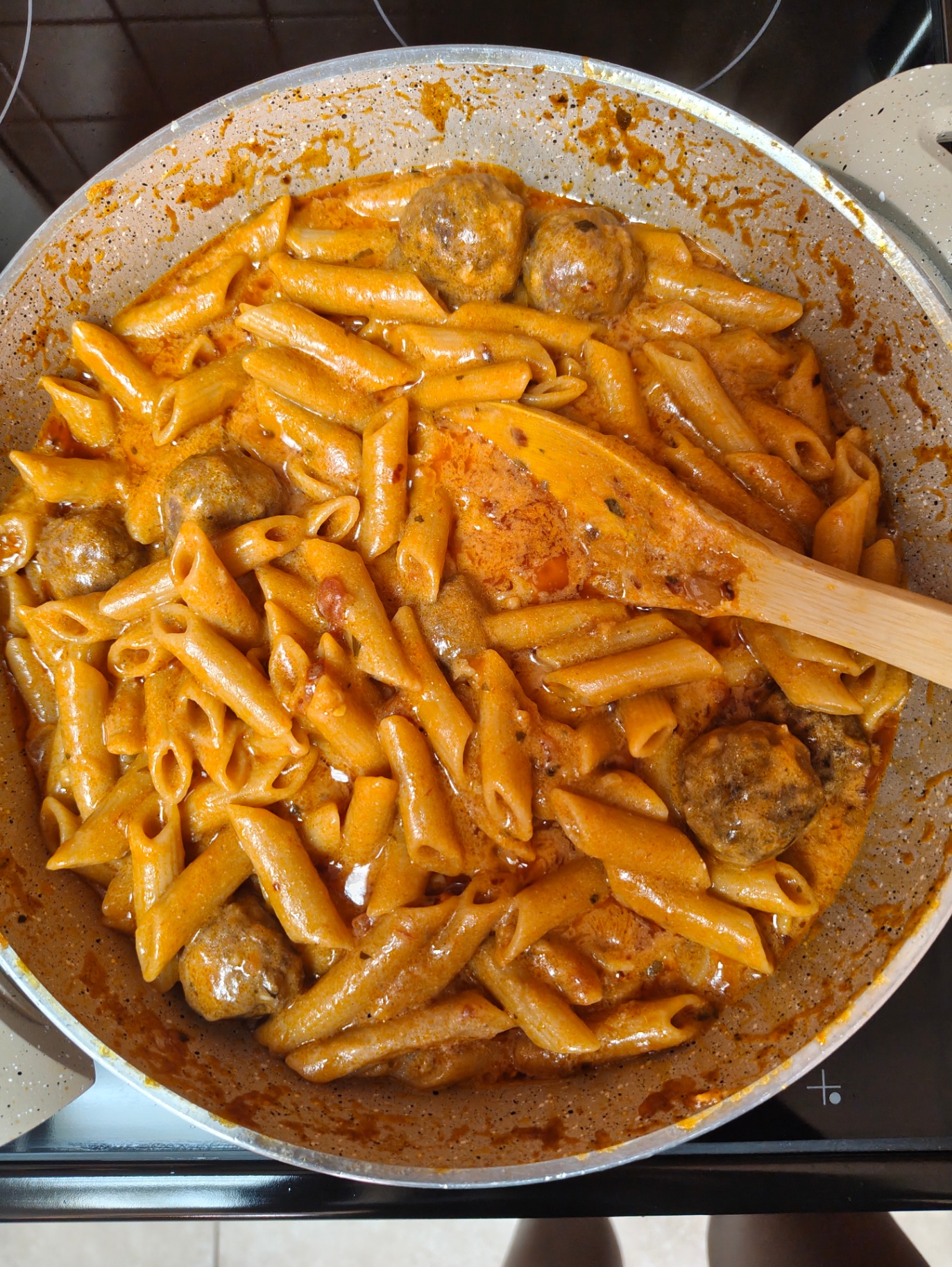 Penne and meatballs mixed through creamy garlic tomato sauce in the pan