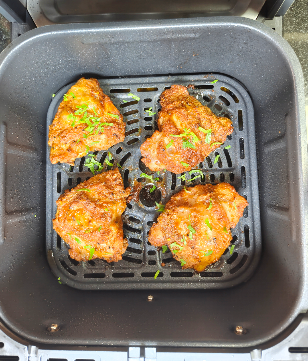 Four cooked chicken thighs browned in an air fryer basket