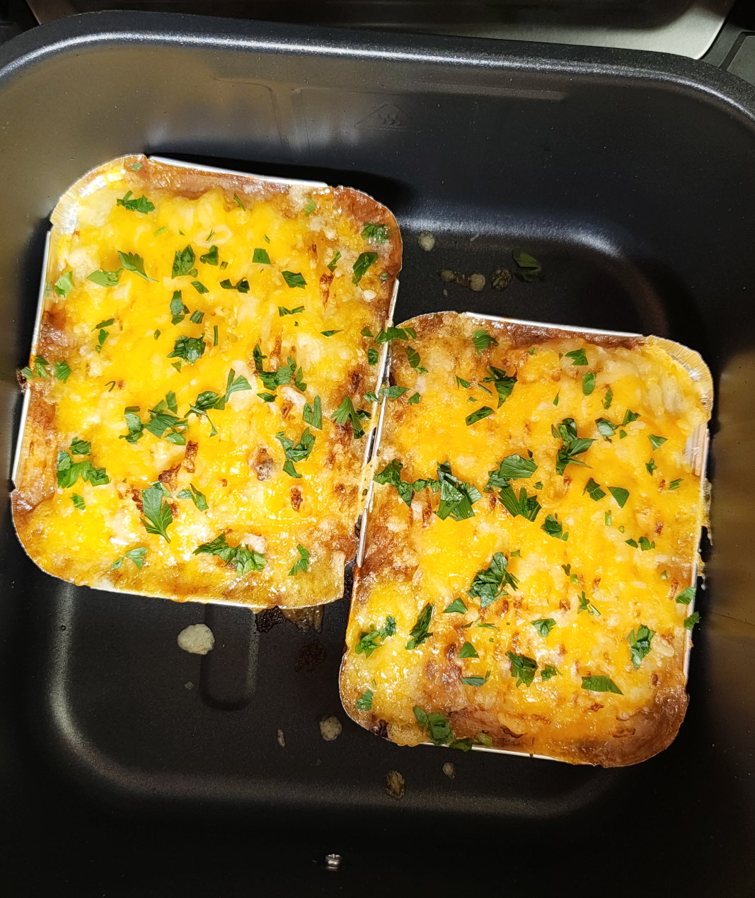 Two cooked dishes in individual foil containers inside an air fryer