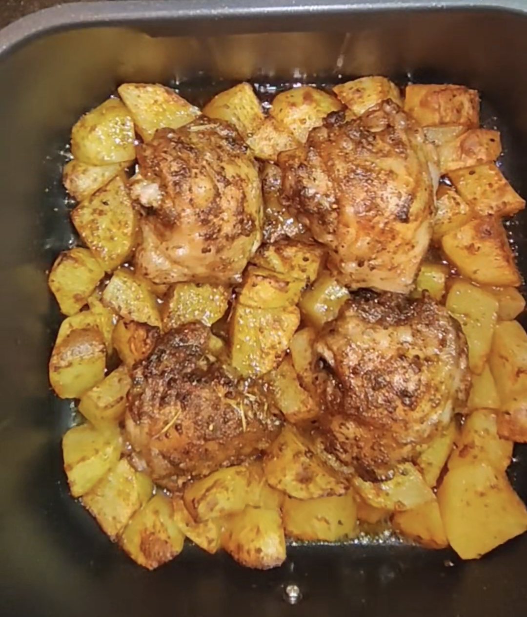 Browned chicken thighs and potatoes in an air fryer basket straight after cooking