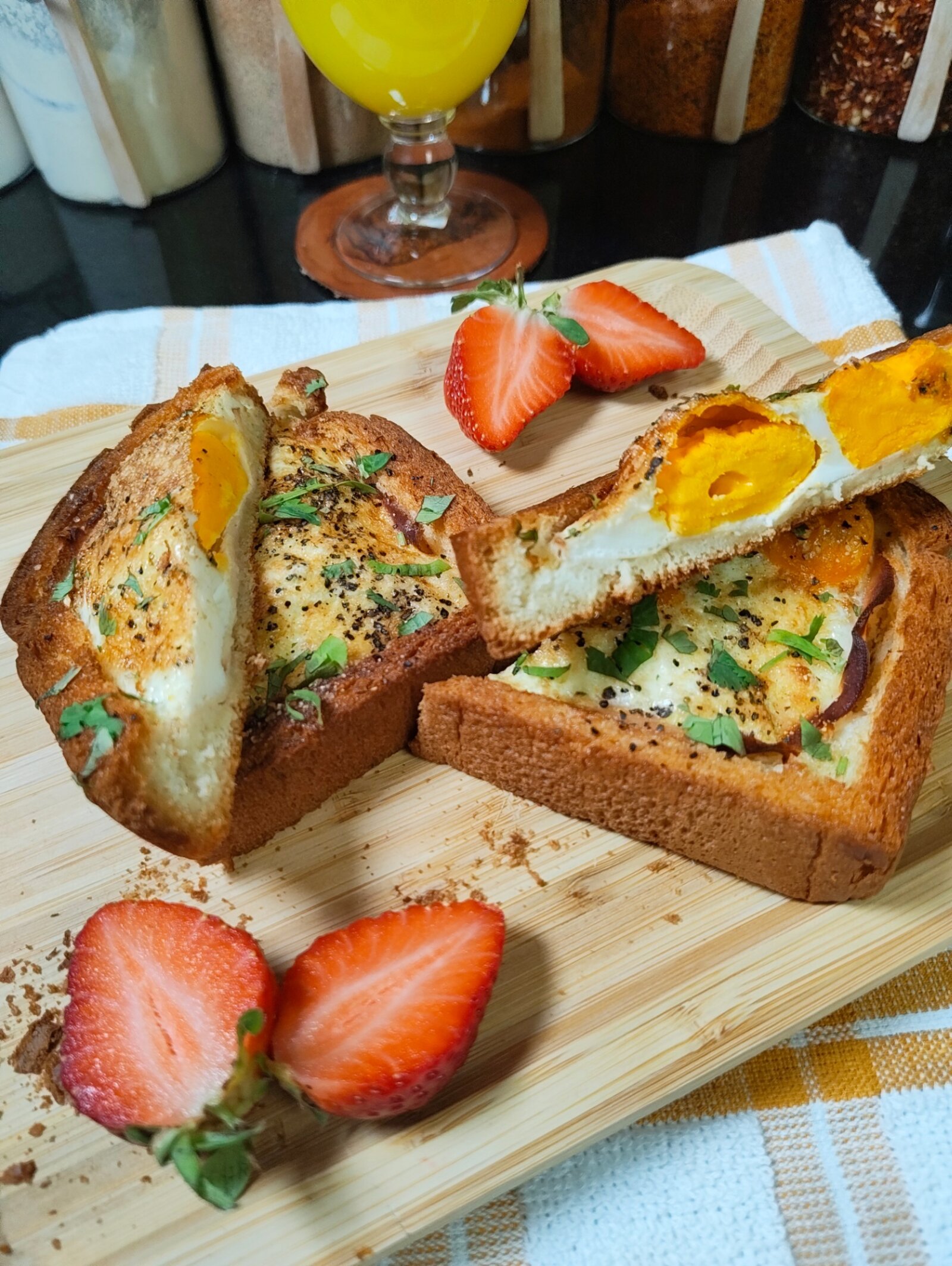 Two air fried eggs in a hole on a wooden board, one piece cut to show the firm yolk inside, with halved strawberries