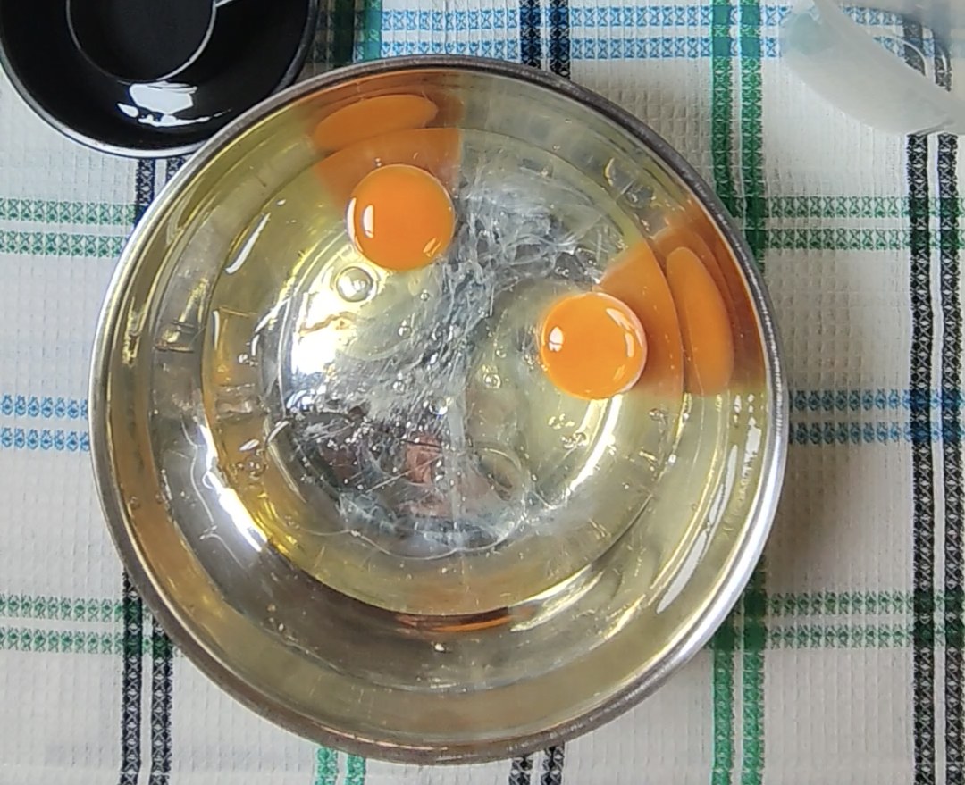 Two eggs with water and vegetable oil in a stainless steel mixing bowl