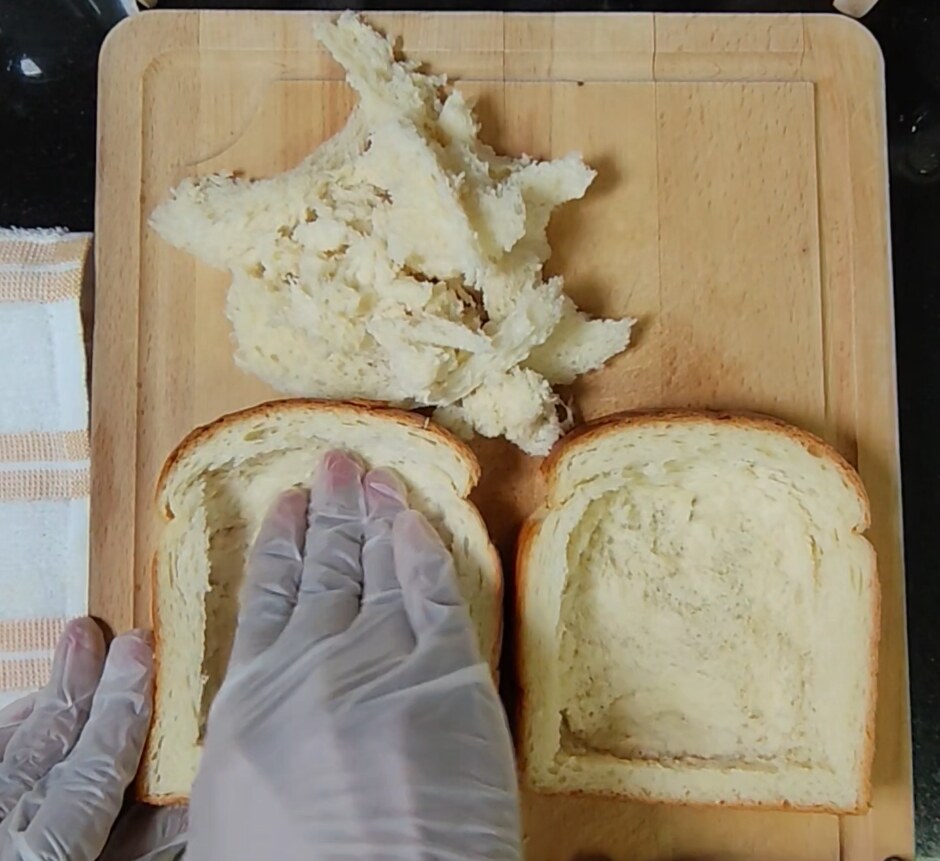 Gloved hand pressing down the centre of a thick slice of brioche beside a second hollowed slice and a pile of removed bread