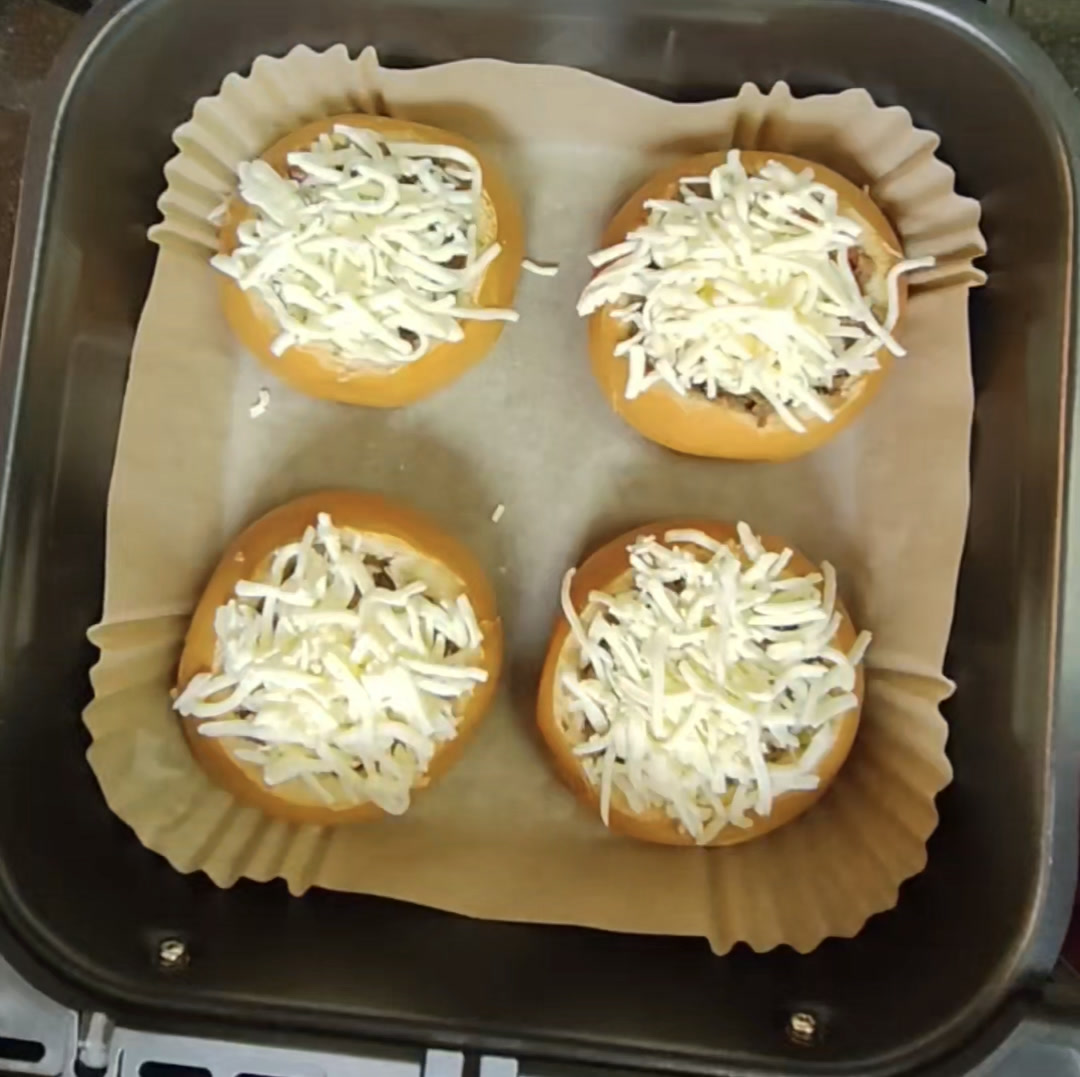 Four filled brioche buns covered with shredded mozzarella in a lined air fryer basket before cooking