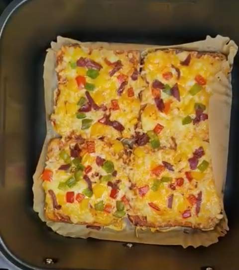 Four bread pizzas with melted cheese and diced peppers inside an air fryer basket
