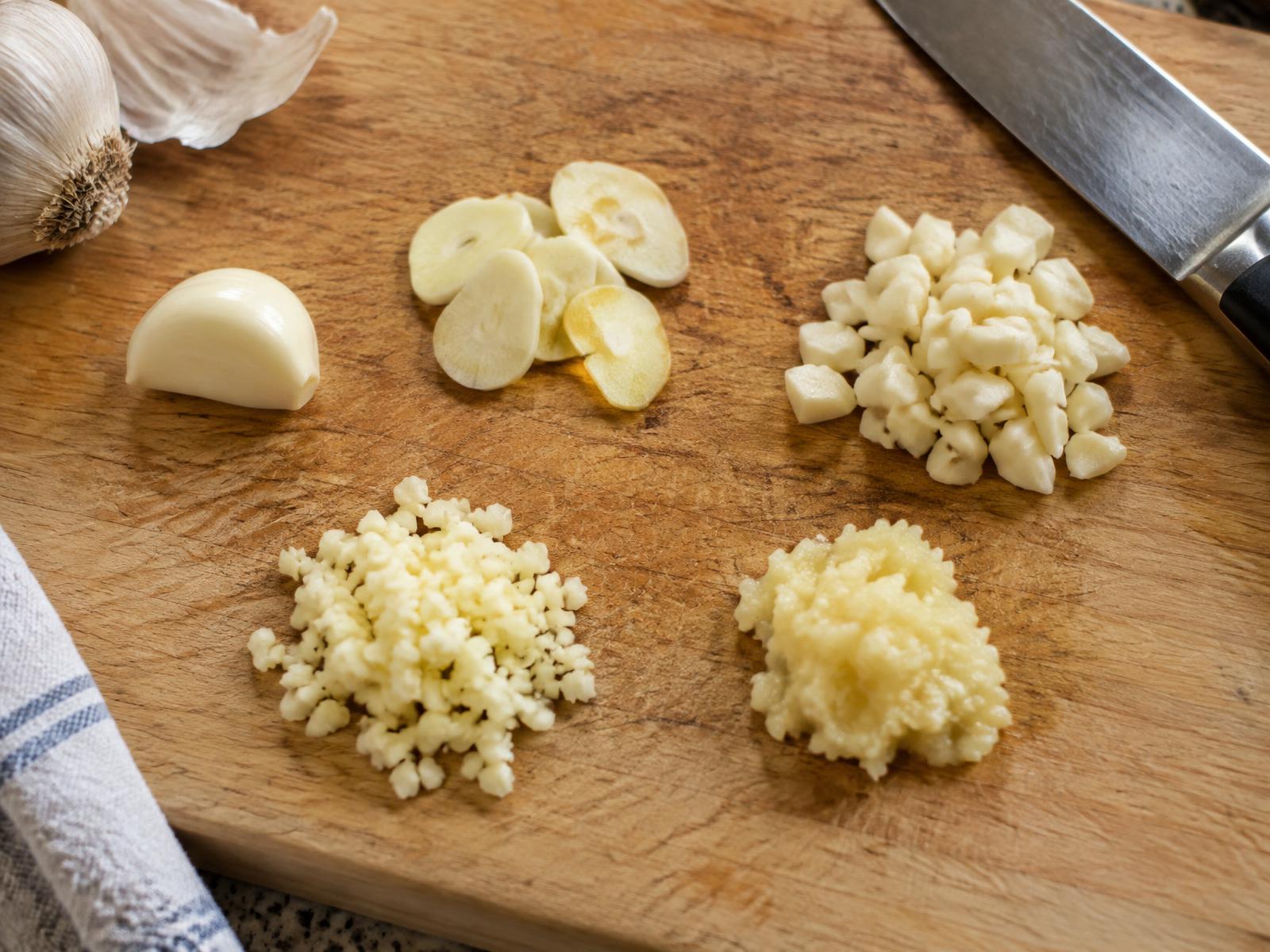 Whole, sliced, chopped, minced and crushed fresh garlic on a chopping board