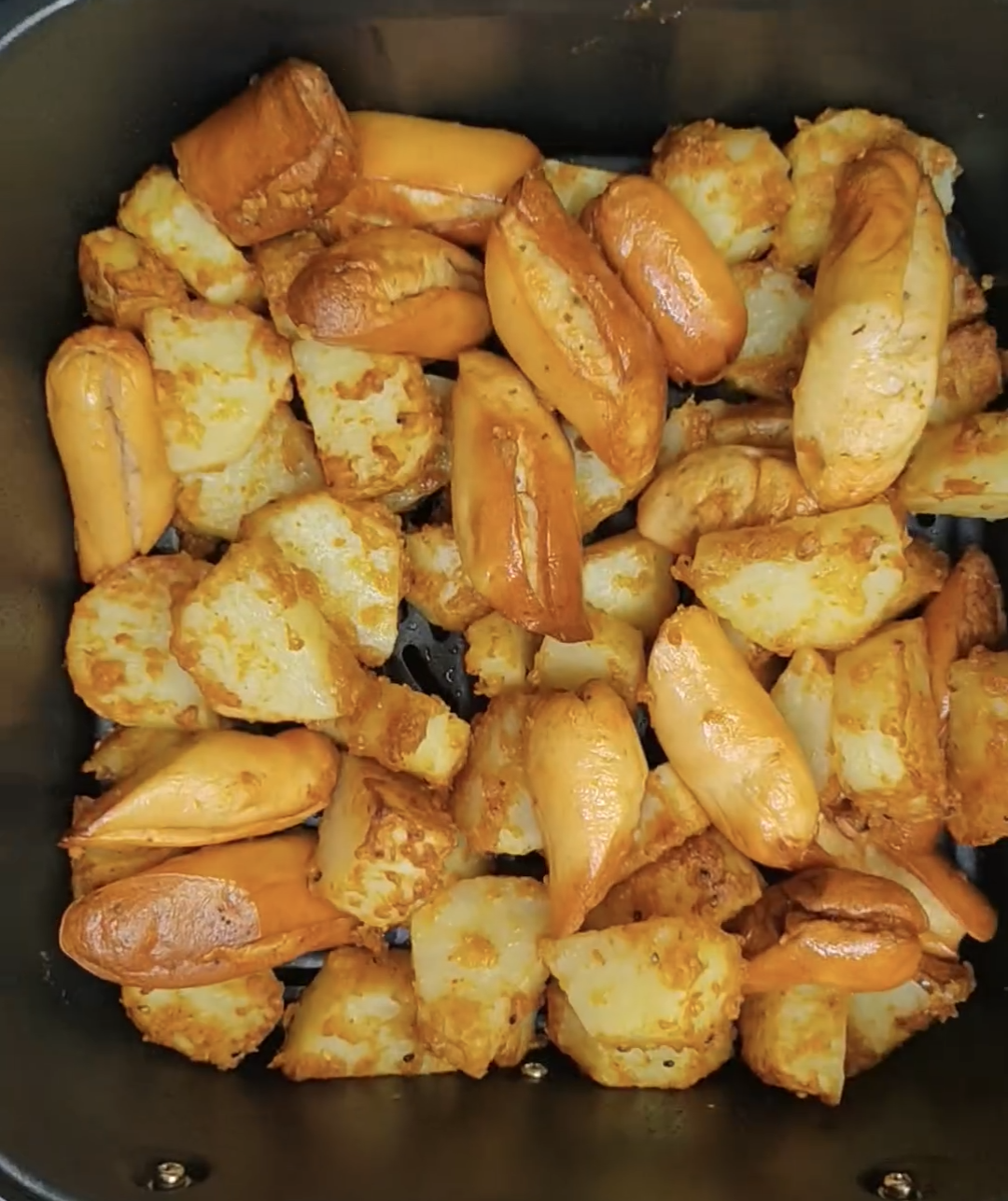 Golden potatoes and browned chicken sausages in the air fryer basket after cooking