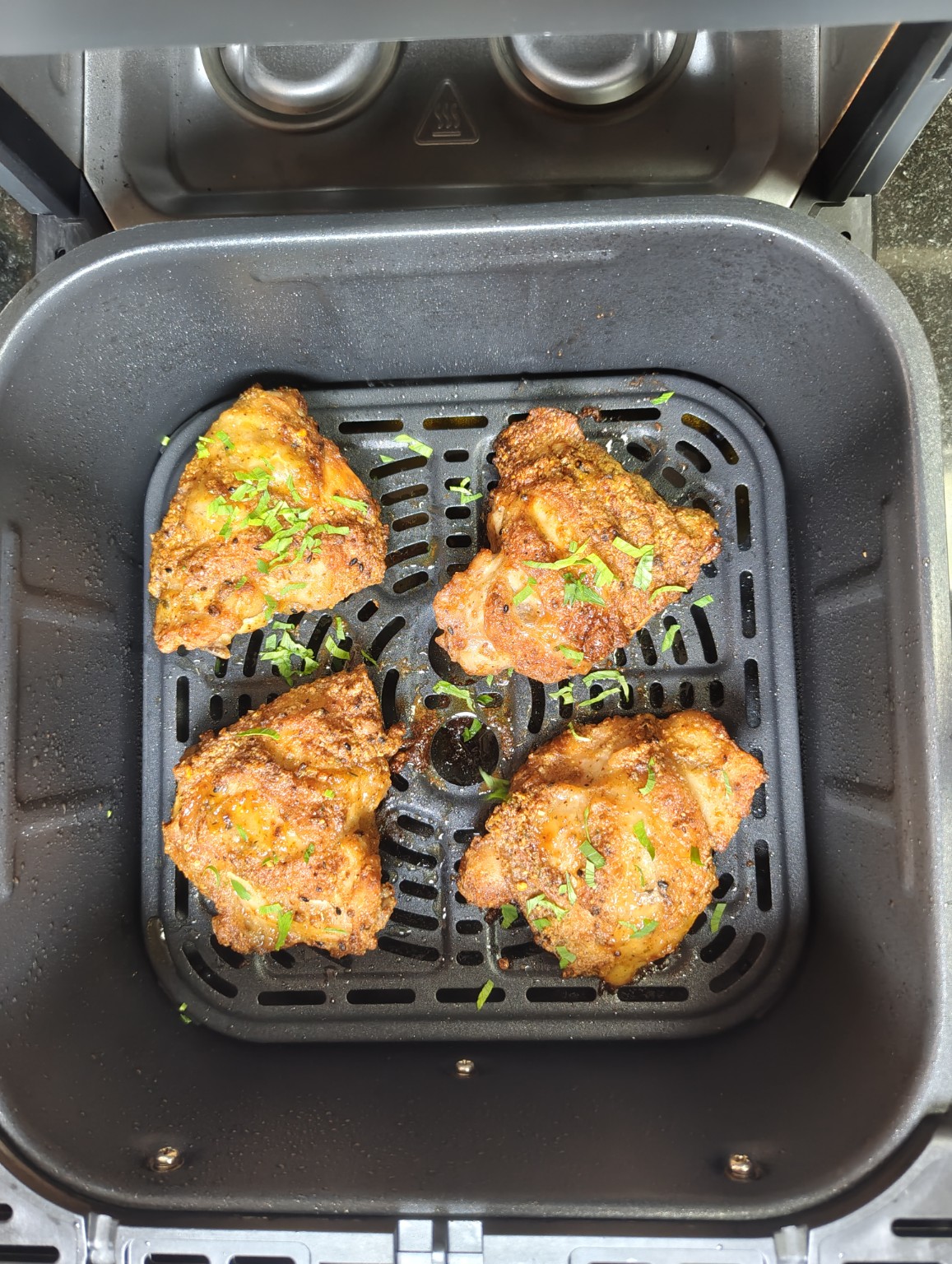 Four cooked chicken thighs in an air fryer basket