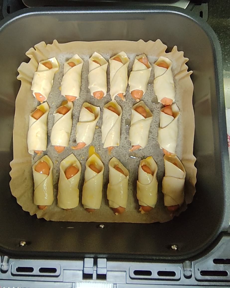 Cocktail chicken sausages wrapped in pastry and arranged in an air fryer basket before cooking