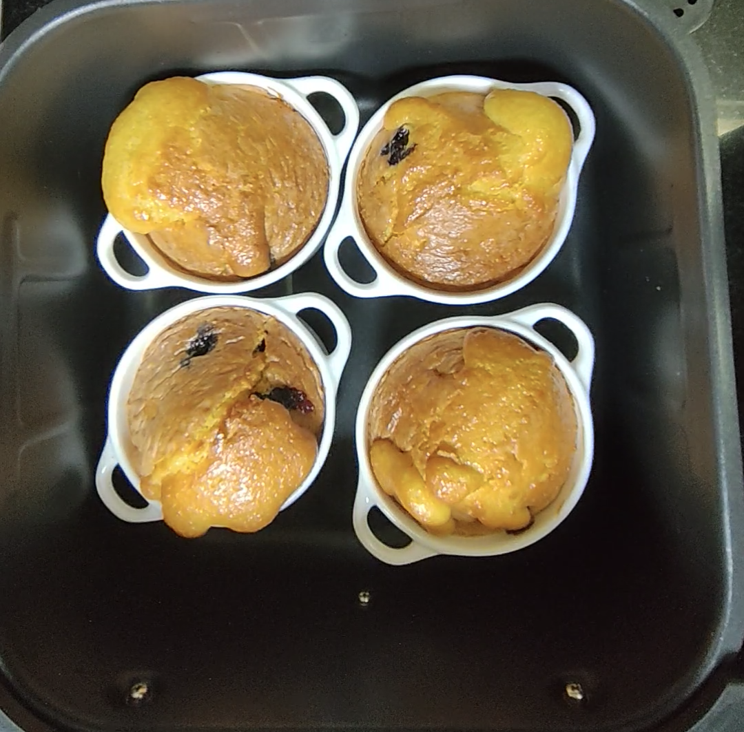 Four golden blueberry lemon muffins risen in white ramekins in the air fryer basket