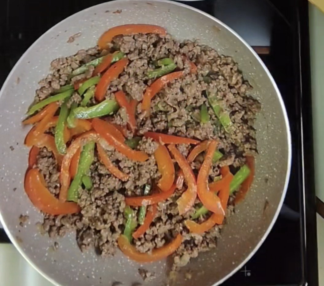 Browned minced beef with sliced red and green bell peppers in a light-coloured pan