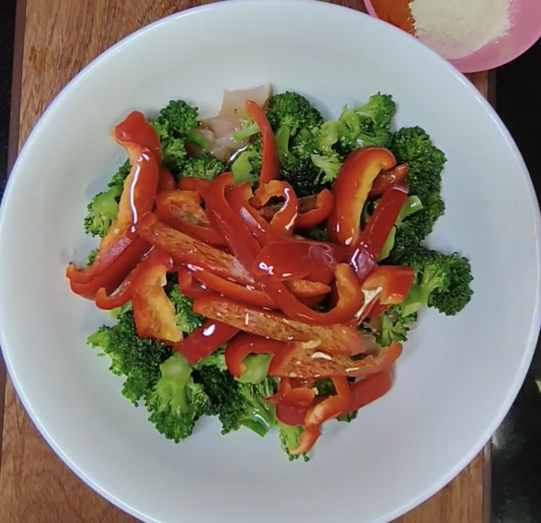 Broccoli florets and sliced red bell pepper with chicken in a white bowl, ready to be seasoned