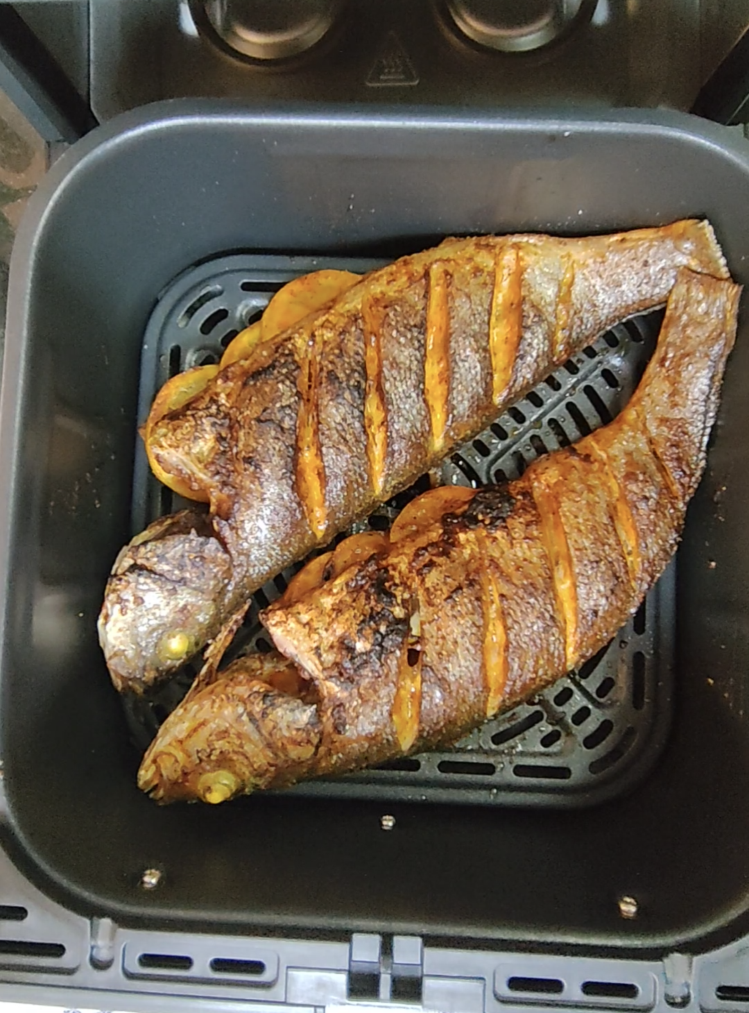 Two whole cooked fish in an air fryer basket