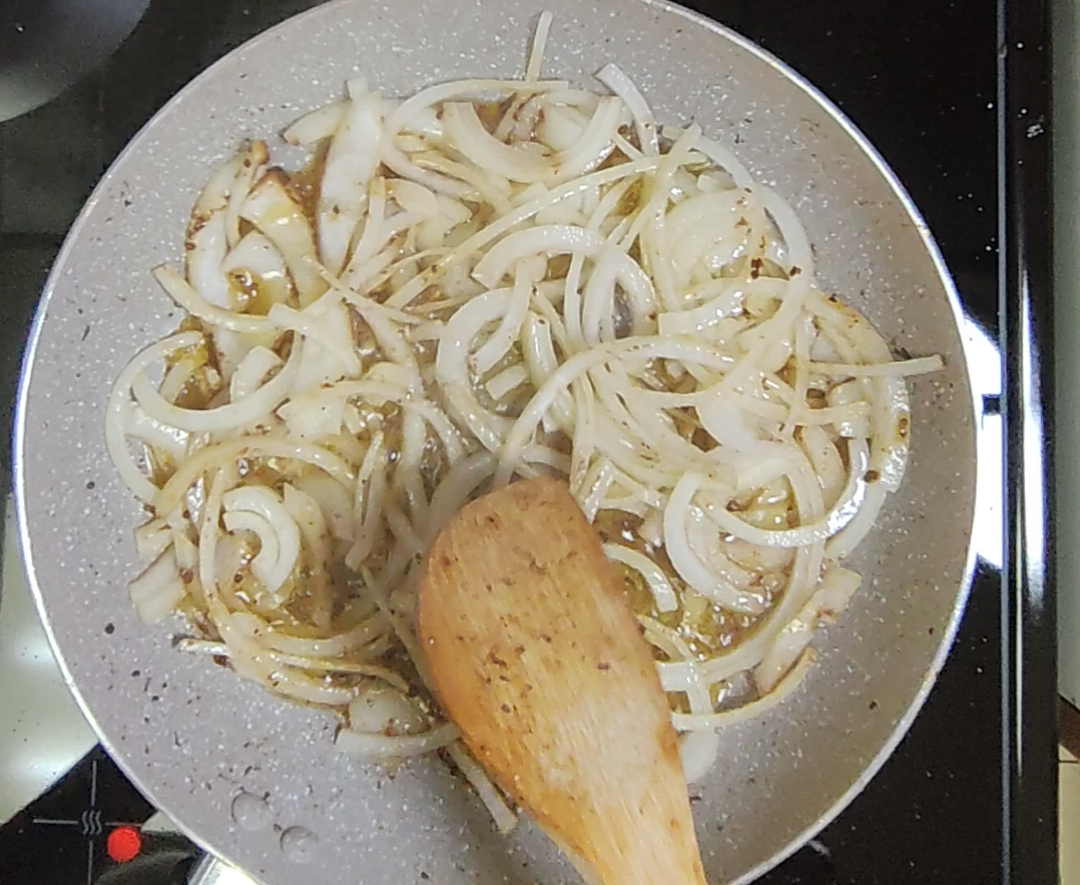 Sliced white onions softening in a light-coloured frying pan with a wooden spoon