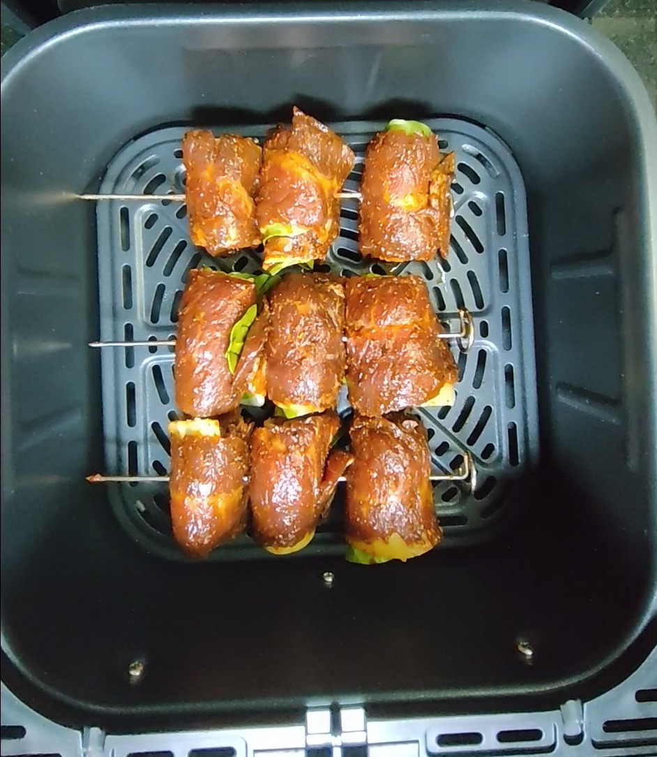 Prepared spinach and mozzarella stuffed beef rolls threaded onto metal skewers in the air fryer basket before cooking