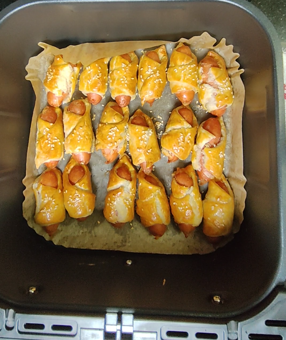 Golden mini sausage pastries sprinkled with sesame seeds in an air fryer basket