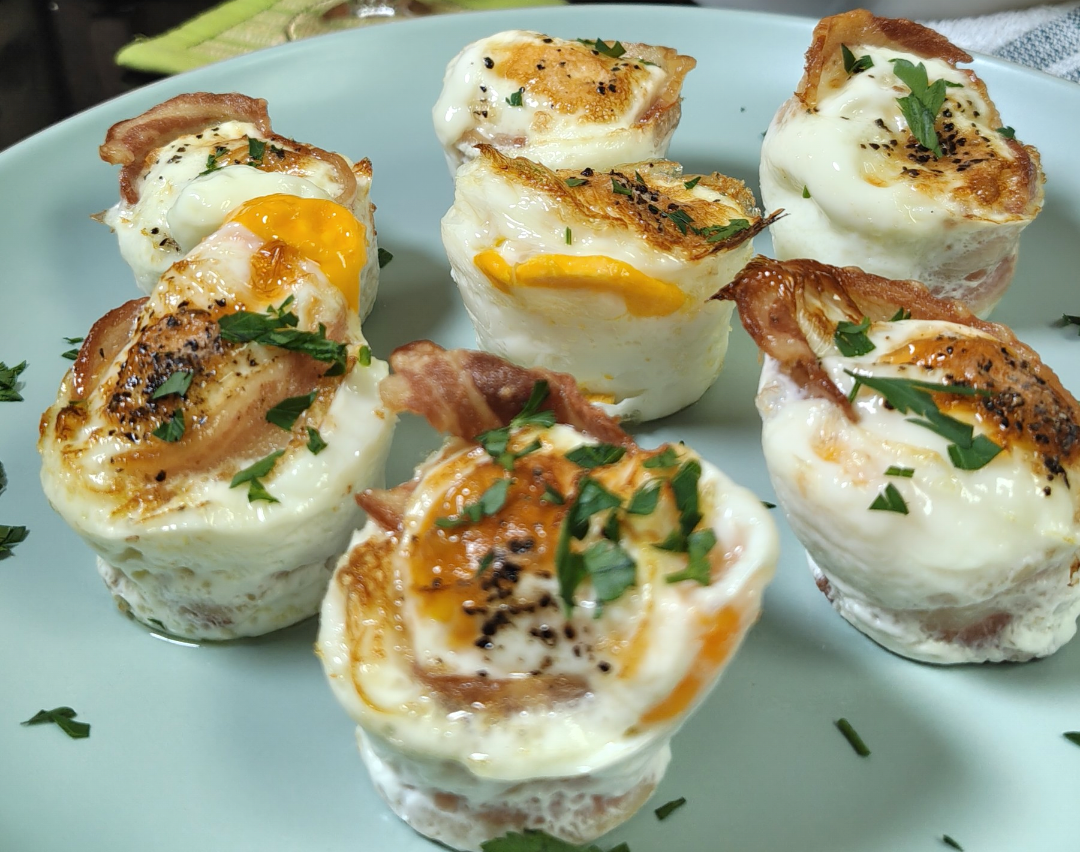 Air fryer bacon and egg cups on a pale blue plate, garnished with fresh parsley and black pepper