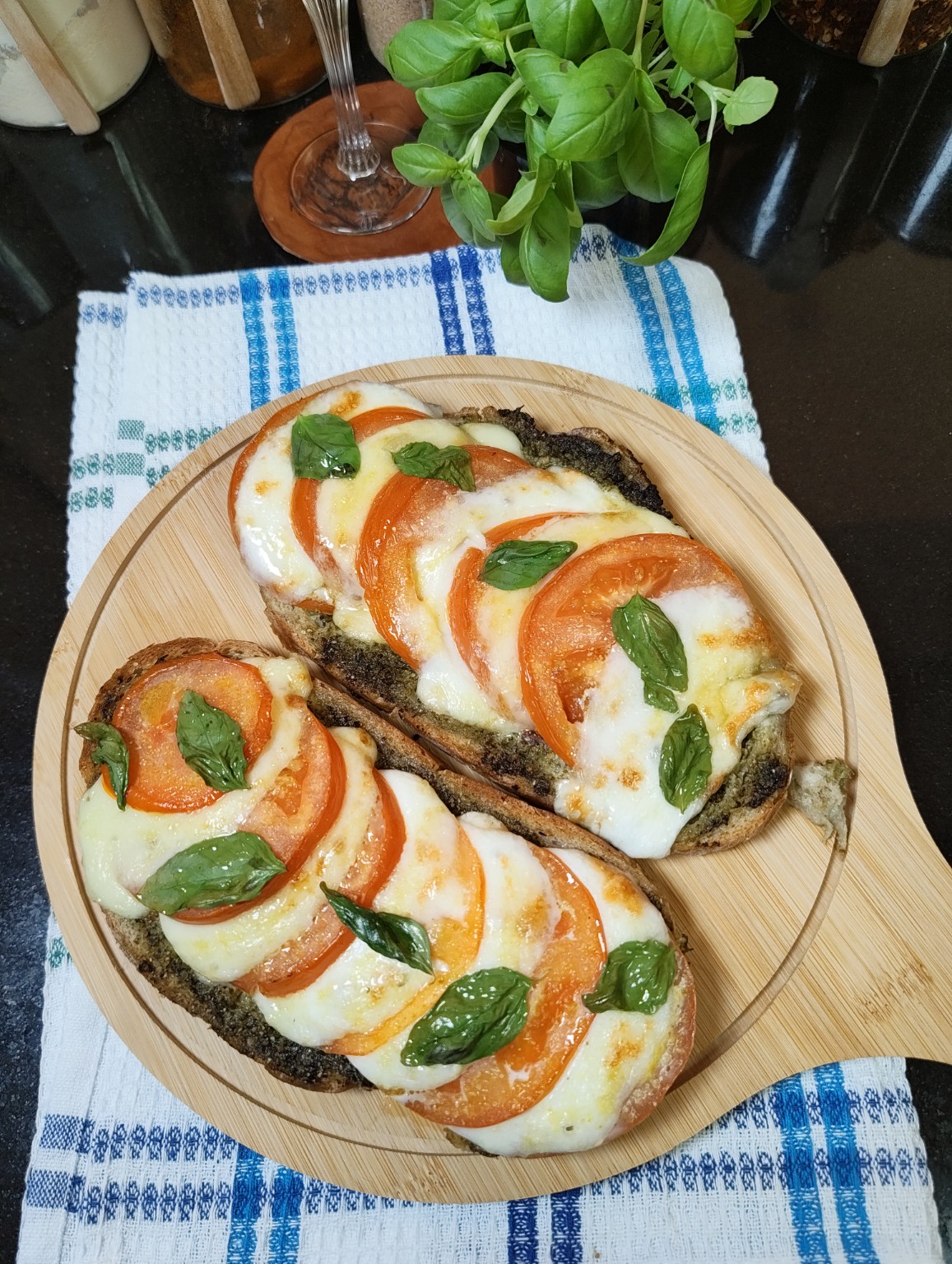 Two open toasts topped with tomato, melted mozzarella and basil