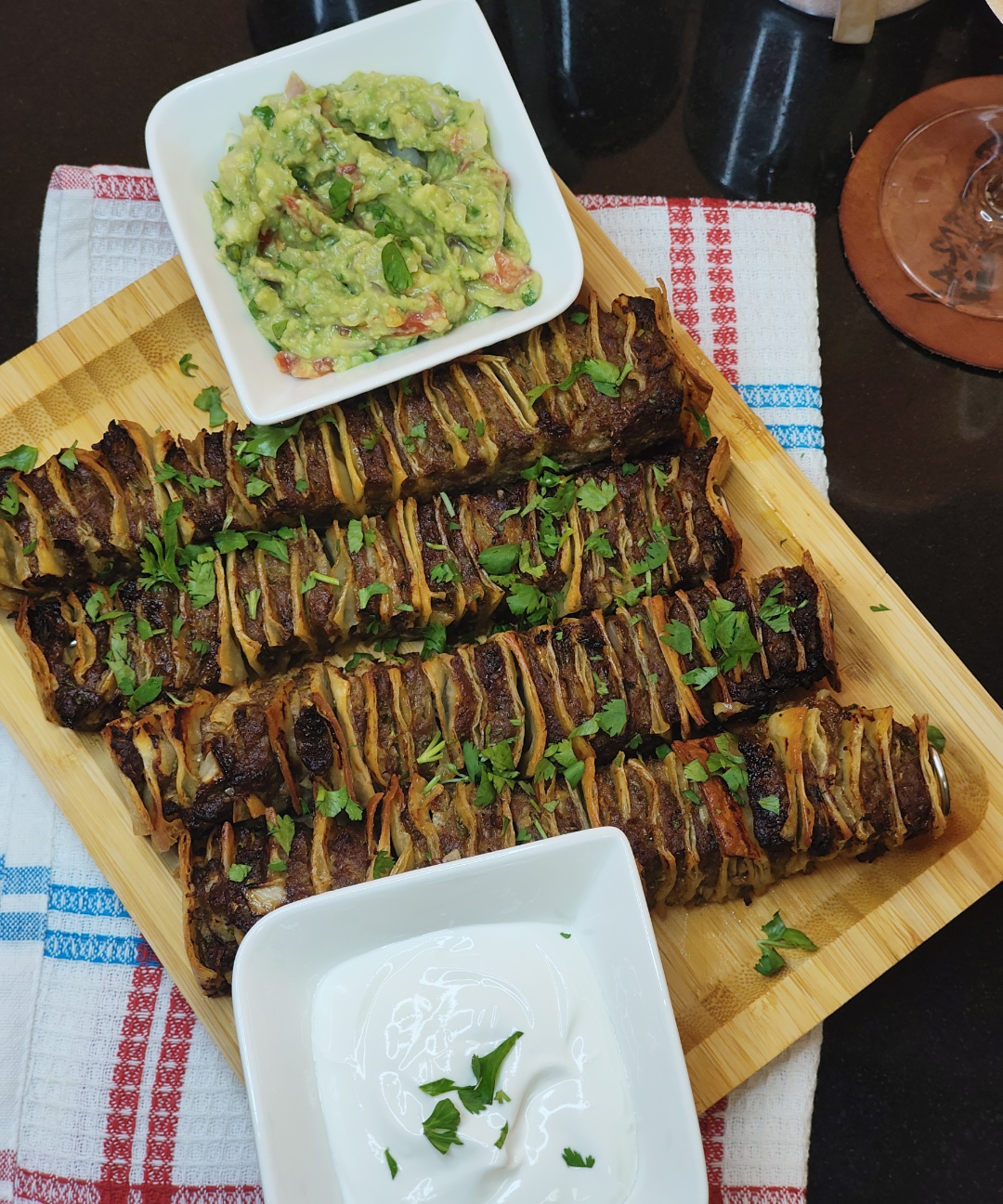 Overhead view of the finished beef and tortilla skewers on a serving board with guacamole and sour cream