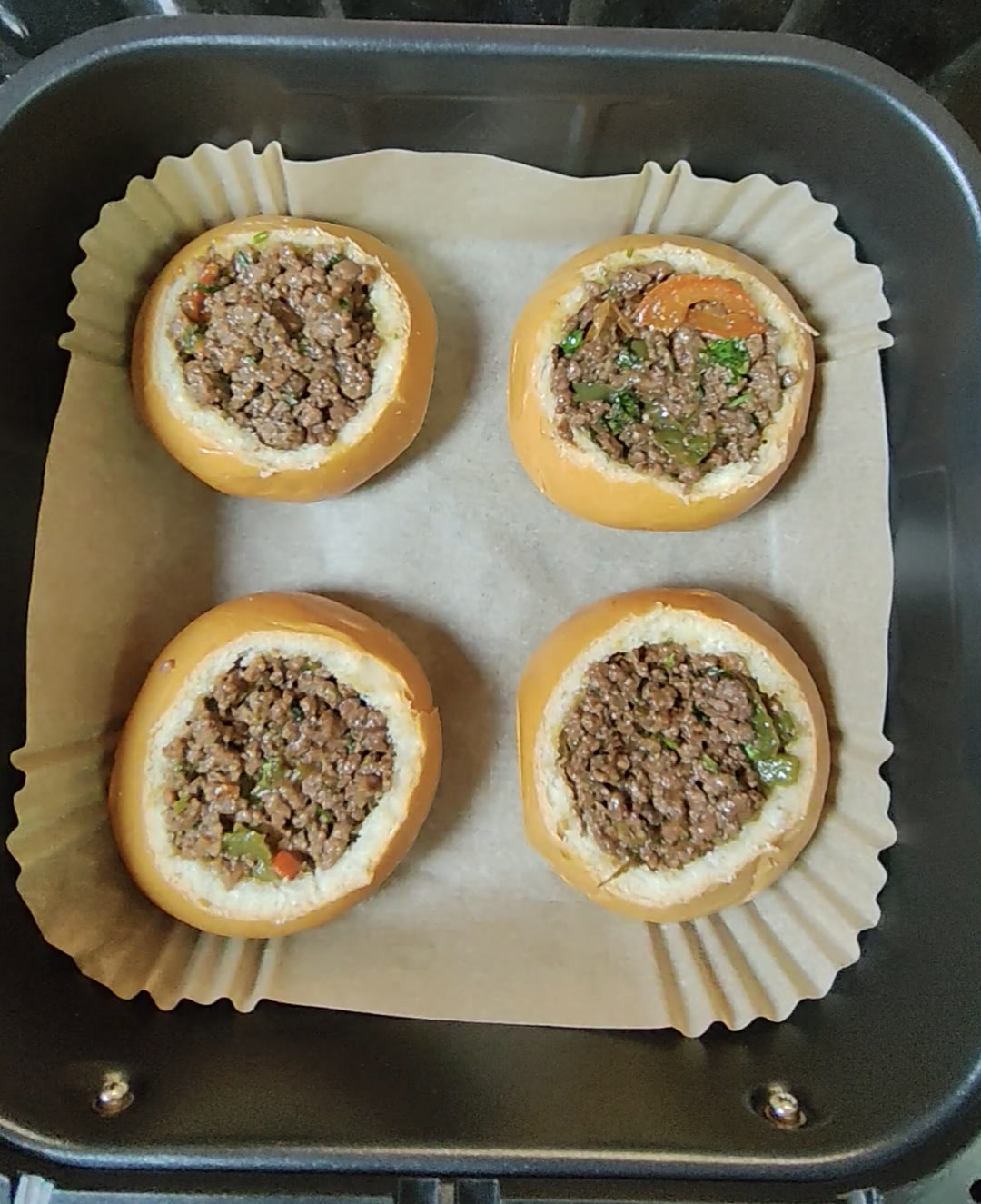 Four hollowed brioche buns filled with minced beef, sitting in a lined air fryer basket