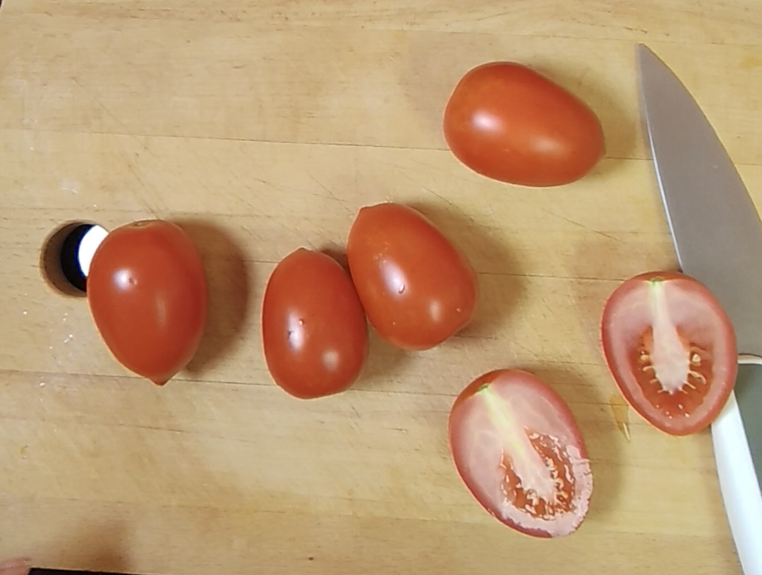 Red tomatoes on a wooden chopping board beside a knife, with one tomato cut in half to show the inside
