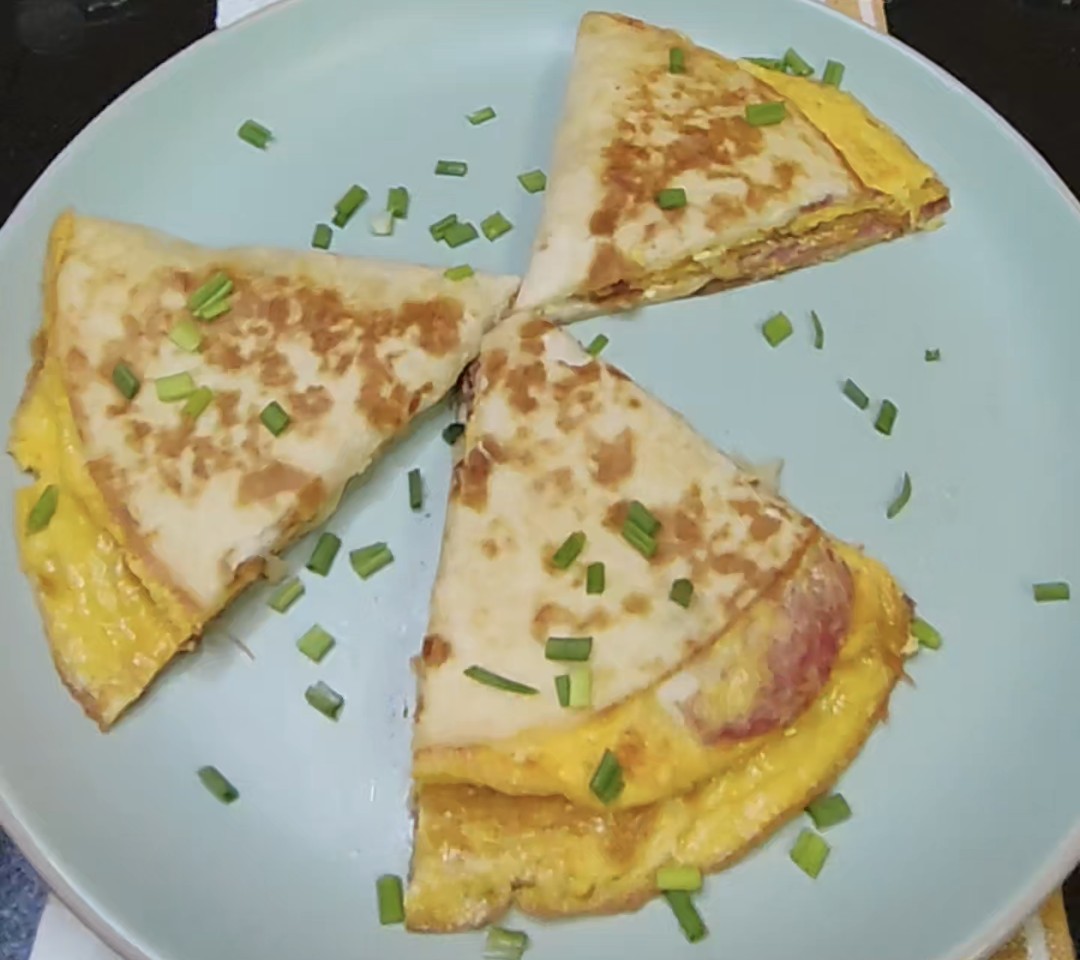 Cheesy egg and salami breakfast tortilla cut into golden triangles and garnished with green onions