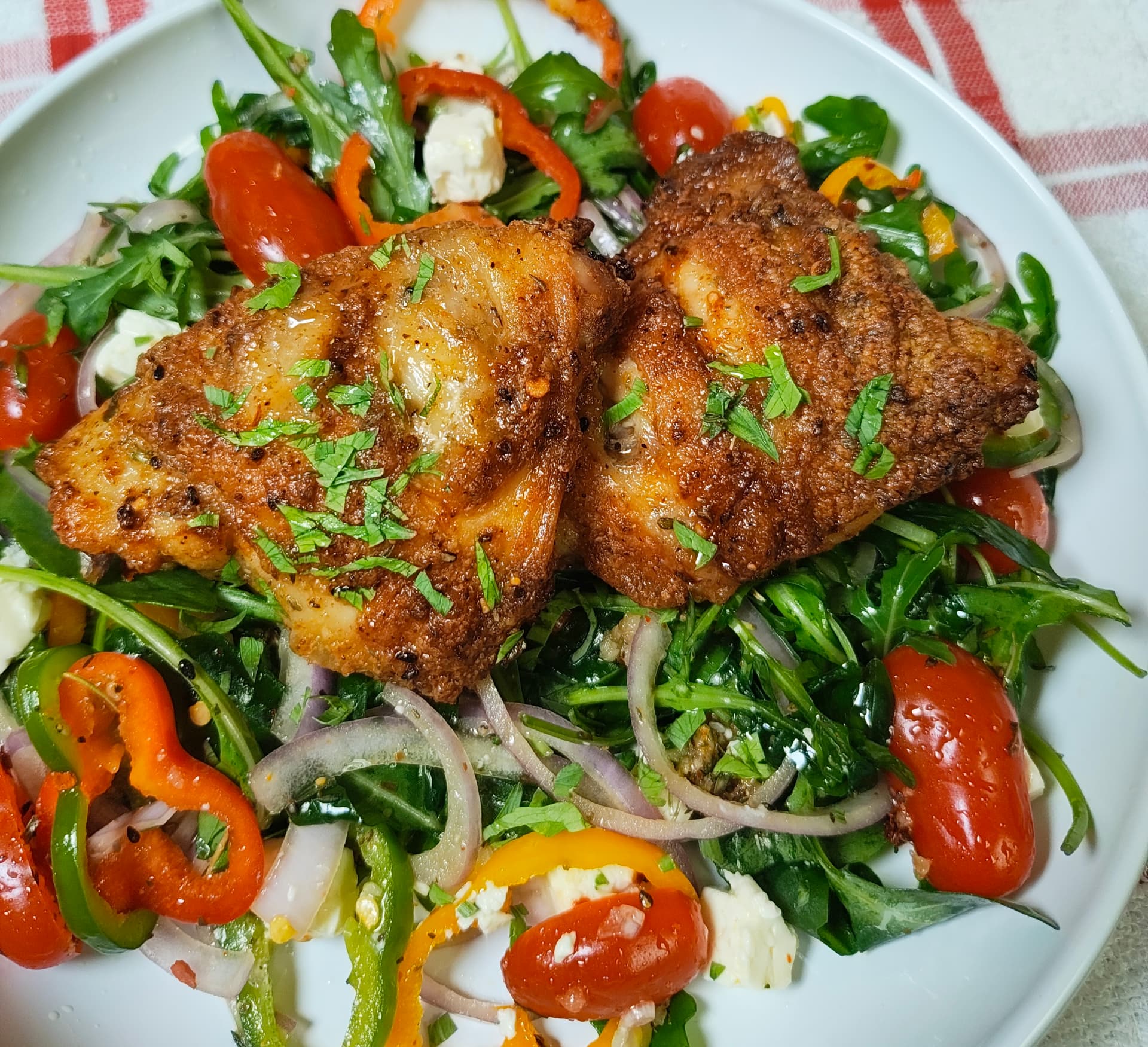 Overhead view of crispy air fryer chicken thighs served on a fresh rocca salad with peppers, tomatoes, red onion and feta