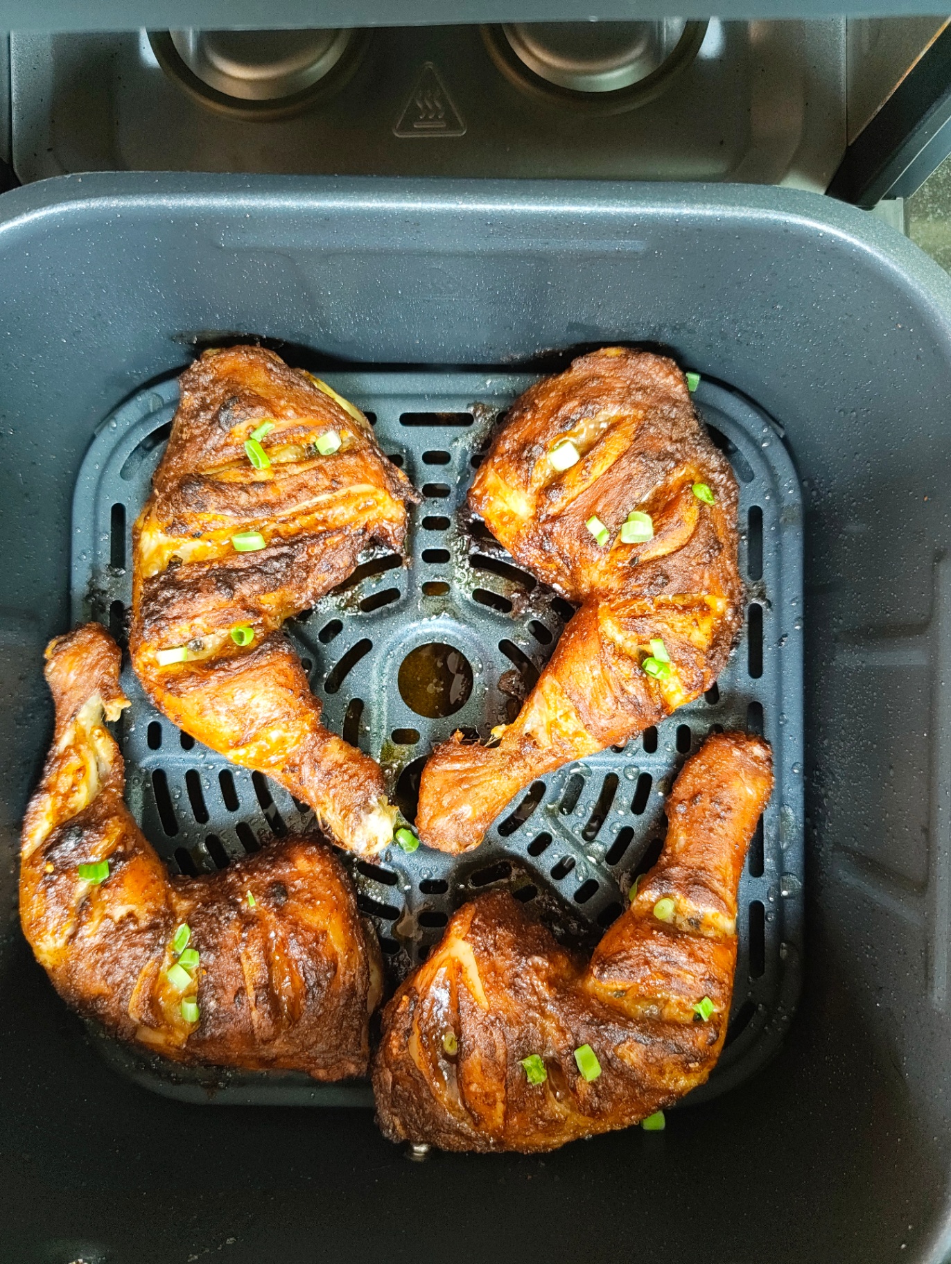 Well-browned crispy chicken leg quarters in an air fryer basket, garnished with spring onion